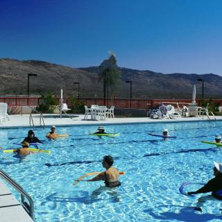 A group of people enjoying a swim in an outdoor pool with mountains in the background.