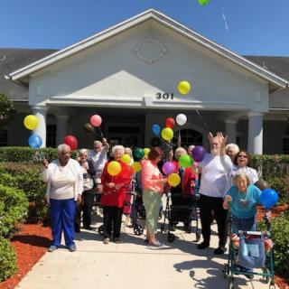 A joyful group of people celebrating outside with colorful balloons in front of a building.