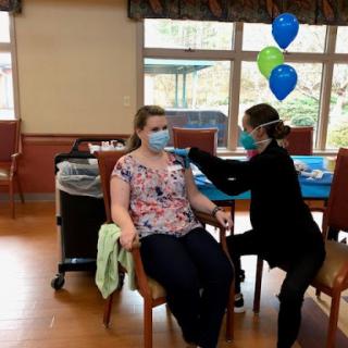 A nurse administers a vaccine to a patient in a healthcare setting, surrounded by decorations.