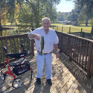 A senior man proudly displaying his catch while enjoying a sunny day by the lake.