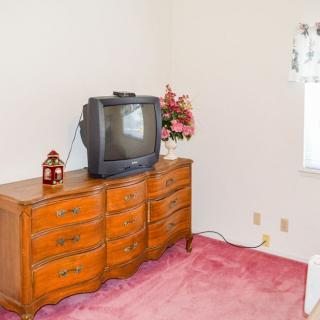 A vintage bedroom setup with a CRT television atop a wooden dresser, complemented by pink carpeting and decorative items.