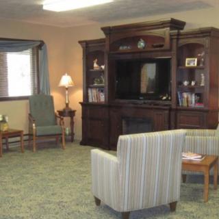 A cozy living room with a television cabinet, upholstered chairs, and a lamp.