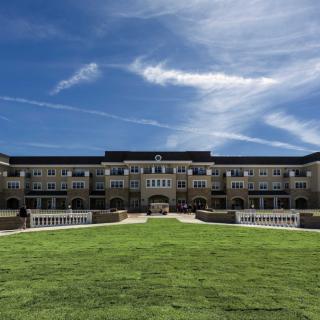 A grand building on a college campus with a wide grassy lawn and a blue sky above.
