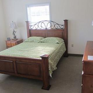 A neatly arranged bedroom featuring a wooden bed frame with green bedding and a matching nightstand.