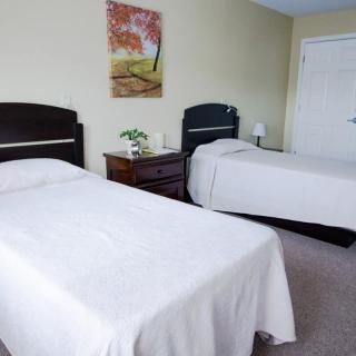 A cozy bedroom featuring two single beds with white bedspreads, a nightstand with a lamp and decorative items, and a painting on the wall.
