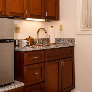 A kitchen area featuring wooden cabinets, a small refrigerator, and a granite countertop with a sink.