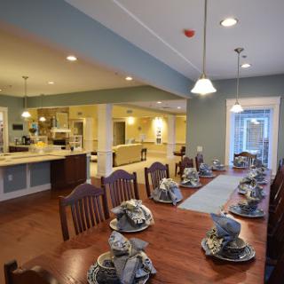A beautifully arranged dining room with a long table set for a meal, showcasing modern design and an open kitchen layout.