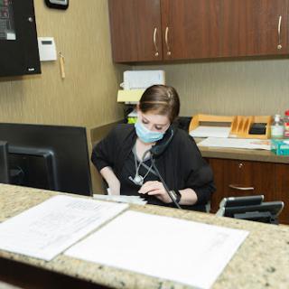 A receptionist in a medical office, wearing a mask while working at a computer.