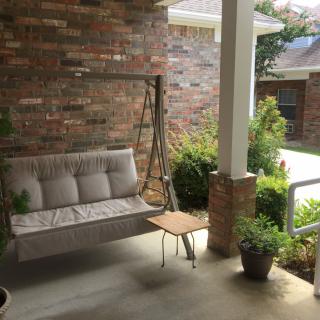 A cozy porch with a swing, small table, and potted plants.