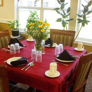 A dining table set for six with a red tablecloth, black napkins, and a floral centerpiece.