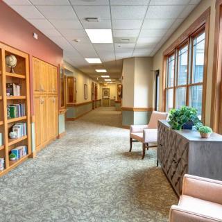 A well-lit hallway with a bookshelf, chairs, and indoor plants.