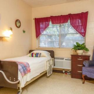 A cozy bedroom with a single bed, decorated with bright curtains and a plant on the dresser.
