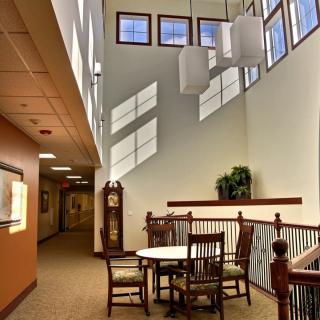 A well-lit interior space with wooden chairs and a table, featuring large windows allowing natural light to flood in.
