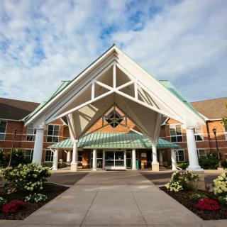 A well-maintained building entrance with landscaped gardens under a partly cloudy sky.