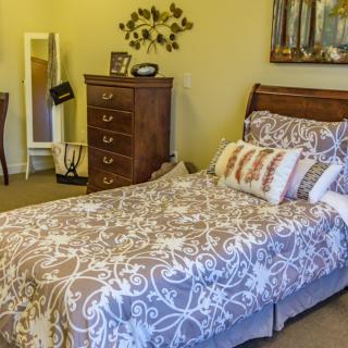 A cozy bedroom with a neatly made bed, wooden dresser, and decorative elements.