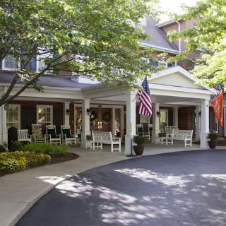 A welcoming entrance to a building with a spacious porch, surrounded by trees and landscaped greenery.