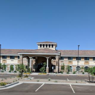 A modern building with an arched entrance and a surrounding parking lot under a clear blue sky.