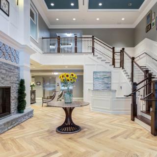 A spacious and luxurious foyer with elegant staircase, wooden flooring, and a central table with sunflowers.