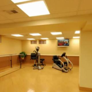 A small indoor gym with exercise equipment including a treadmill and an elliptical machine, along with a television mounted on the wall.