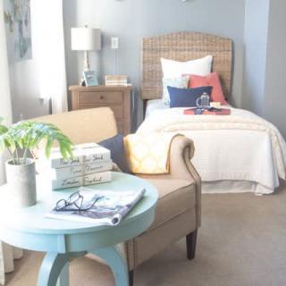 A cozy bedroom with a single bed, an armchair, and a small side table adorned with books and a plant.