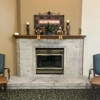 A cozy room with a brick fireplace, decorated mantel, and two chairs.