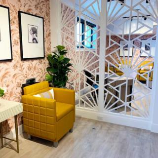 A stylish interior featuring a yellow armchair, framed wall art, plants, and a decorative partition on a wooden floor.