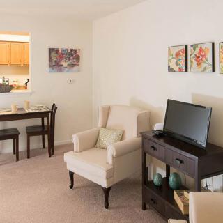A cozy living room with an armchair, TV stand, and small dining area.