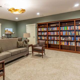 A cozy library room featuring a sofa, armchairs, and extensive bookshelves filled with books.