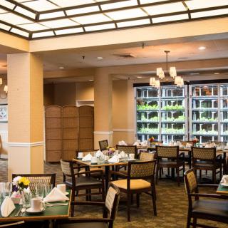A spacious and elegantly decorated dining room with neatly arranged tables and chairs, enhanced by large windows and stylish chandeliers.