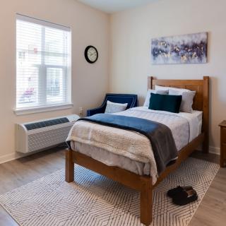 A cozy minimalist bedroom with a single bed, armchair, and natural light from the window.