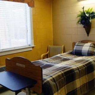 A small hospital room with a single bed, chair, and window.