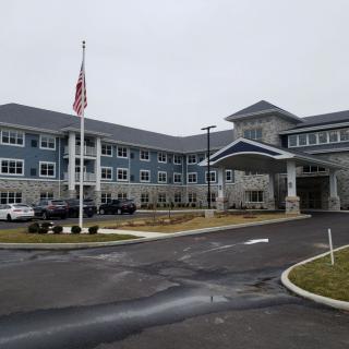 A large building with an American flag in front, surrounded by a parking lot and driveway on a cloudy day.