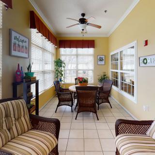 A cozy indoor seating area with wicker furniture, large windows, and a ceiling fan.