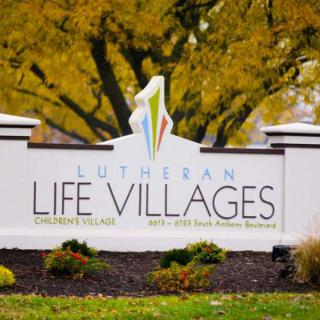 A sign for Lutheran Life Villages set against a backdrop of autumn trees.