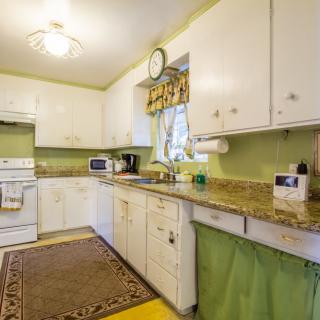 A cozy kitchen with white cabinets and green walls, featuring a granite countertop and retro-style decor.