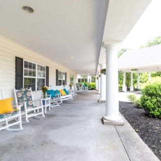 A spacious porch with rocking chairs and decorative pillows, surrounded by columns and greenery.