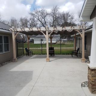 A spacious patio featuring a wooden pergola and outdoor seating, set in a backyard.