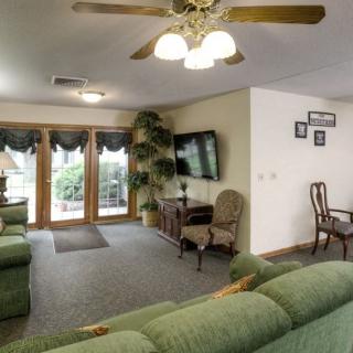 A cozy living room with green sofas, an armchair, a wall-mounted TV, and a ceiling fan.