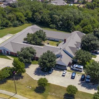 Aerial view of a large building surrounded by trees with a parking lot in the foreground.