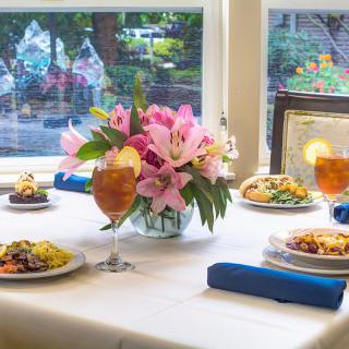 A beautifully set dining table with meals and drinks by the window, featuring a vibrant floral centerpiece.