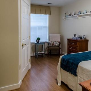 A cozy bedroom with a bed, dresser, and chair situated near a window.