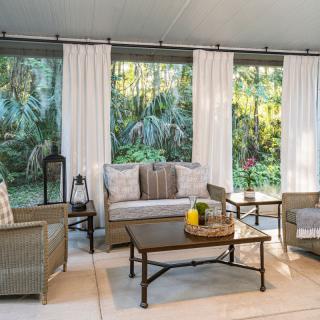 A cozy patio area with comfortable seating, surrounded by lush greenery and natural light.