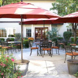 A cozy outdoor patio with tables, chairs, and red umbrellas in a garden setting.