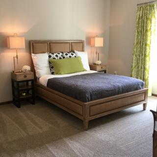 A cozy and modern bedroom with a neatly made bed, flanked by two nightstands and lamps, featuring green curtains and neutral decor.