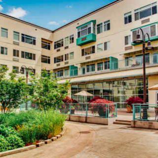 A modern apartment building with a well-maintained courtyard featuring lush vegetation and outdoor seating.