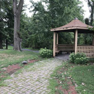A serene garden scene featuring a wooden gazebo surrounded by lush greenery and a brick pathway.