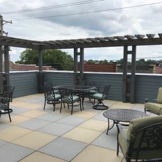 A spacious rooftop patio with comfortable seating under a pergola and a cloudy sky backdrop.