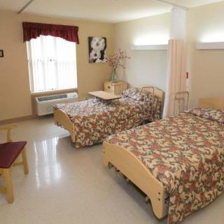 A shared room with two beds, decorated in a floral pattern, featuring a window with curtains and basic furniture.