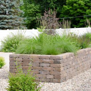 A landscaped garden featuring a brick retaining wall with various plants and greenery.
