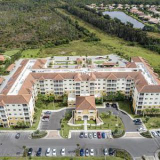 Aerial view of a residential complex with surrounding greenery and a parking lot.